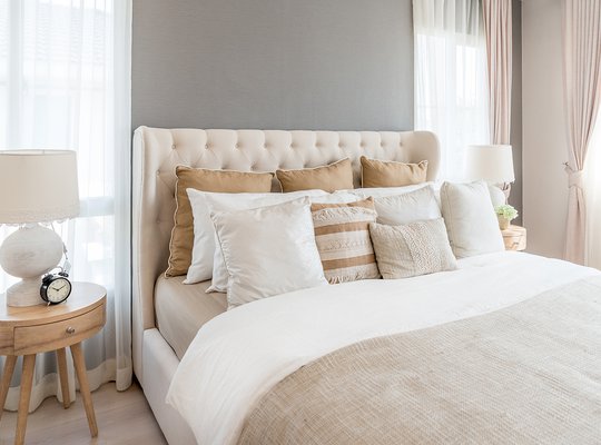 Bedroom in soft light colors. Big comfortable double bed in elegant classic bedroom